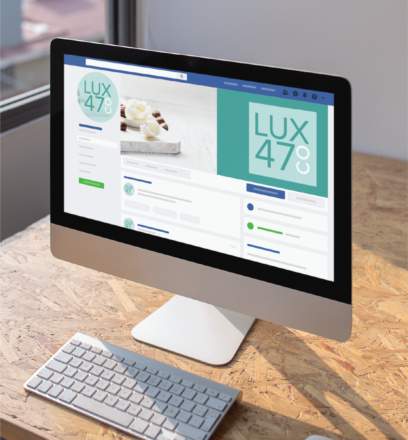 A desktop computer on a wooden desk displays a social media profile page for LUX 47º with a logo and a photo of white candles, showcasing elegant Social Graphics. A wireless keyboard and mouse sit in front of the screen.
