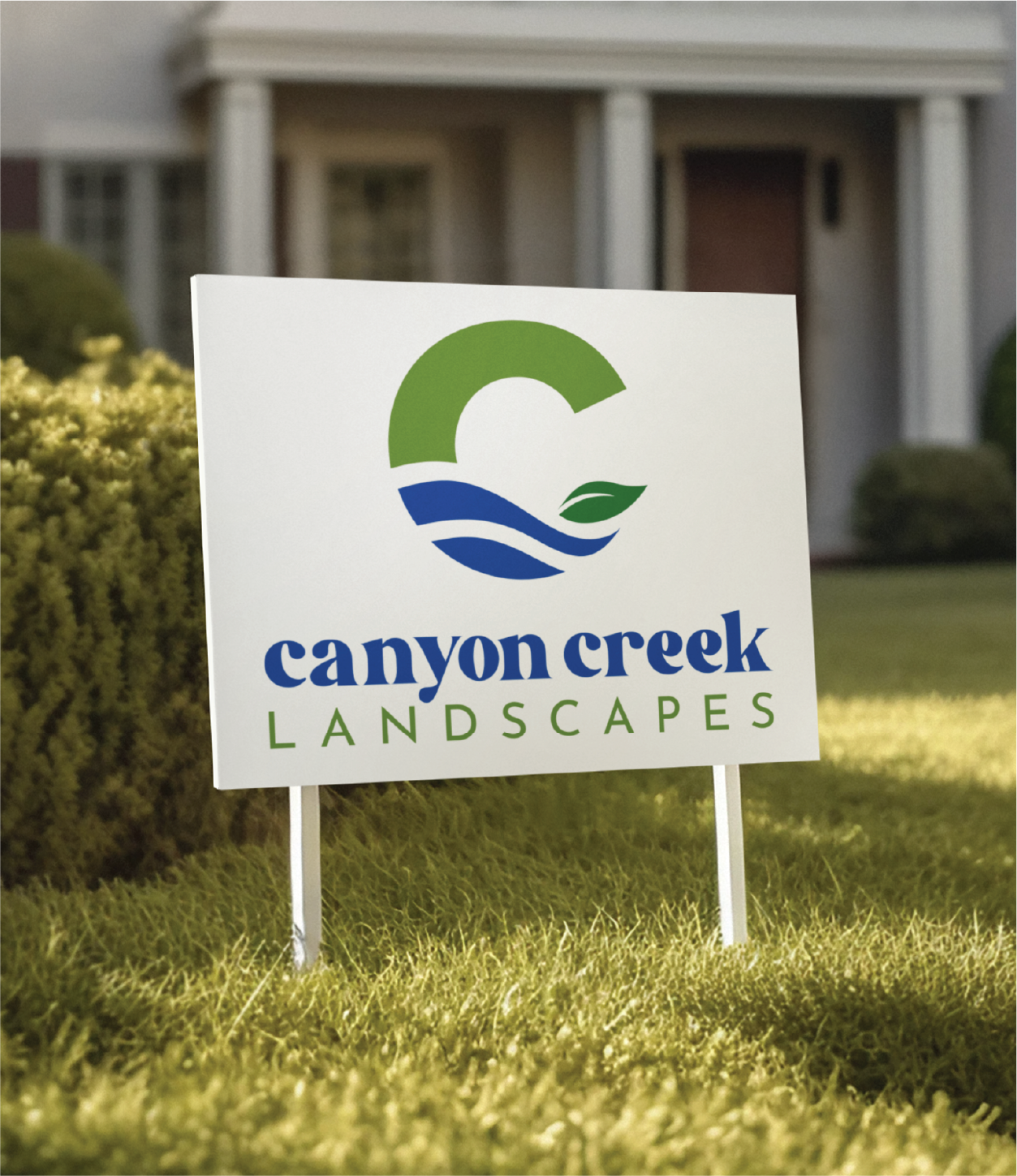 A yard sign with the logo and text Canyon Creek Landscapes, showcasing expert brand design, is displayed on a lawn in front of a house in New Jersey, featuring green, blue, and white colors with a leaf and wave design.