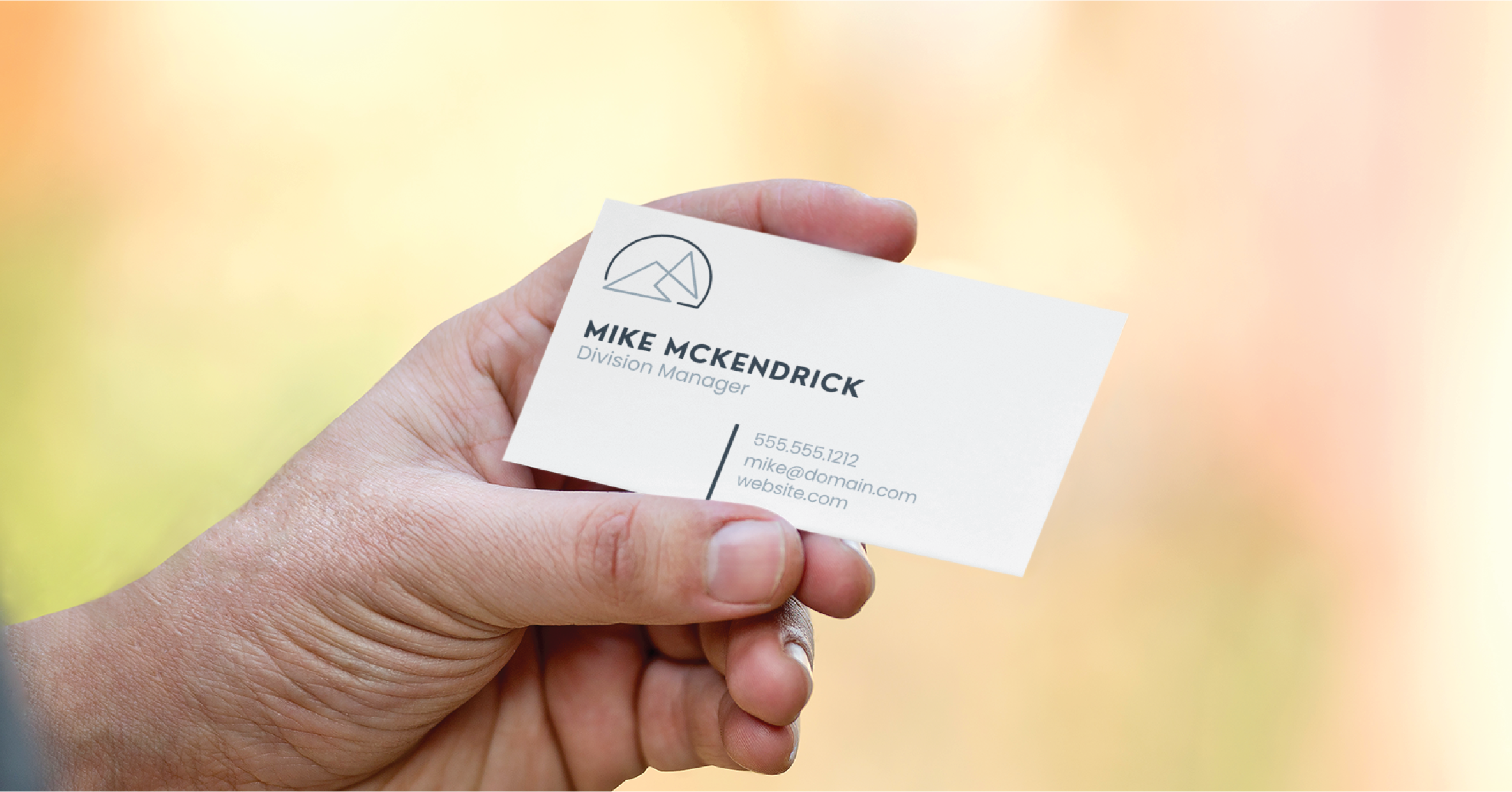A hand holds a business card displaying a logo, the name Mike McKendrick, Division Manager, contact details, and website—showcasing professional Business Card Design for a leading Michigan Business Service against a blurred background.