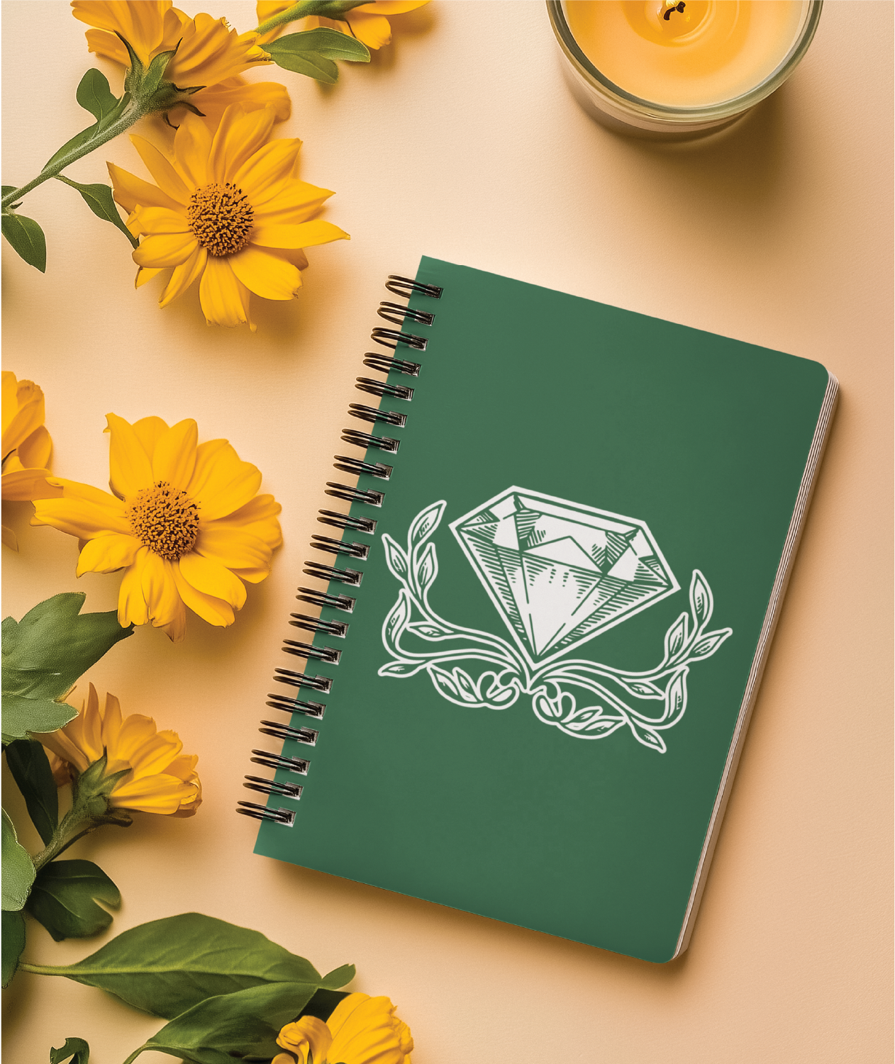 A green spiral notebook with a white diamond and leaves logo design on the cover is placed on a beige surface, surrounded by yellow flowers and a lit yellow candle.