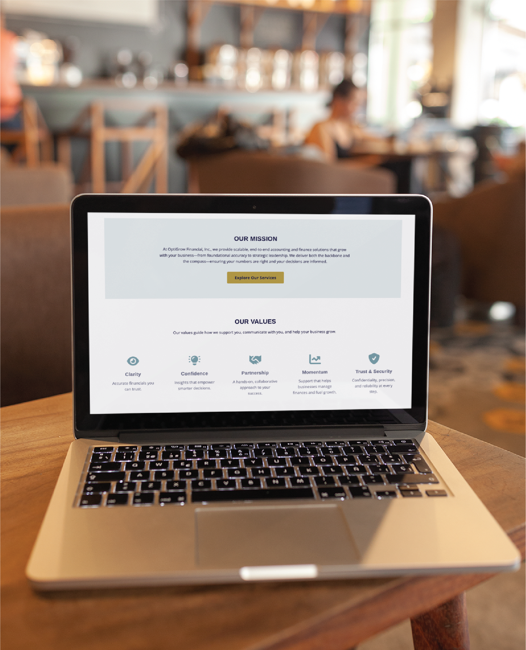 A laptop on a wooden table displays a company’s mission and values page, including care, confidence, partnership, trust, and security. The scene hints at Texas roots and expertise in website design amid a blurred café background.