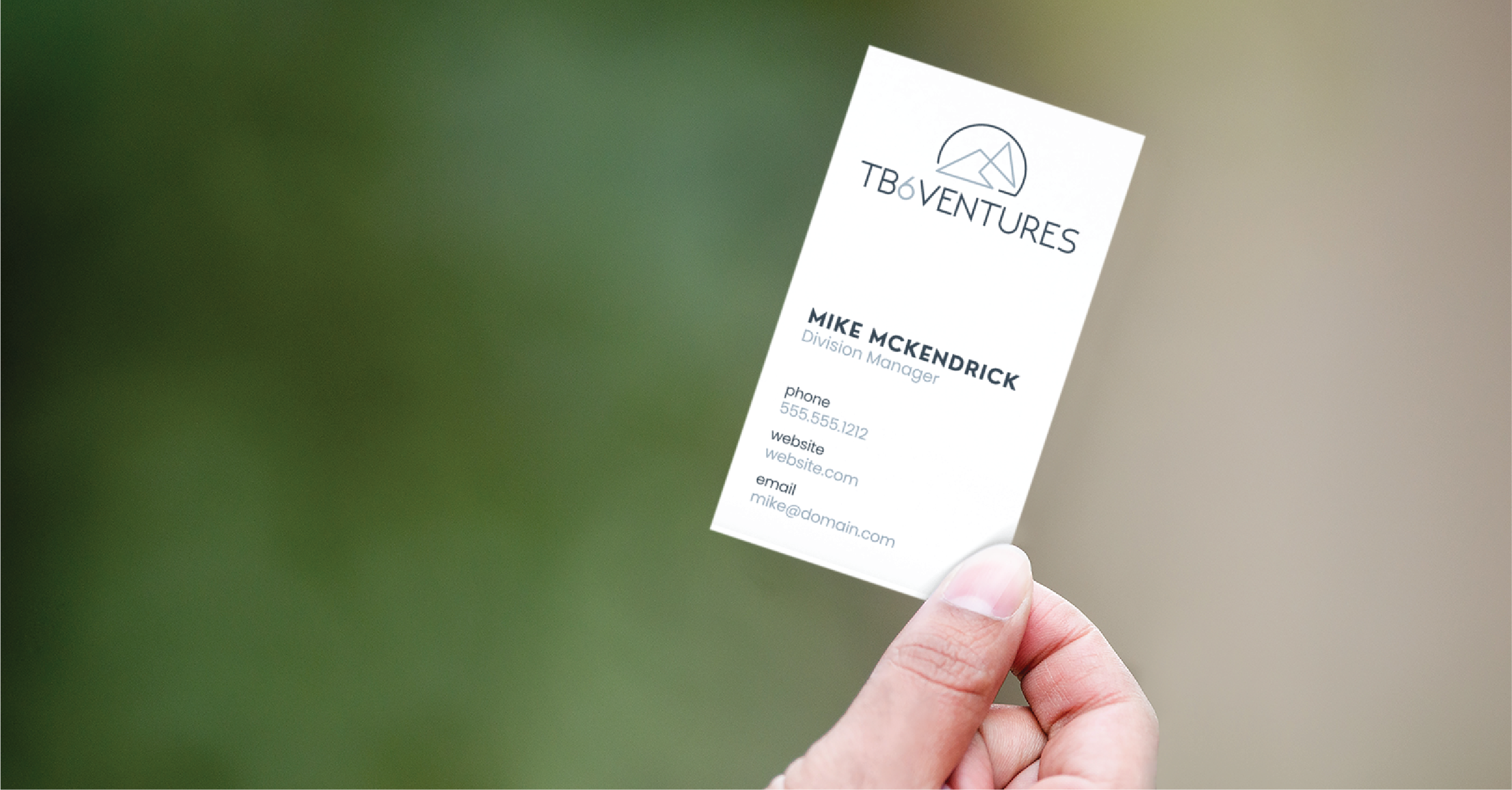 A hand holds a white business card for TB Ventures, showcasing sleek business card design for Division Manager Mike McKendrick and contact details, set against a blurred green background—representing top business service in Michigan.