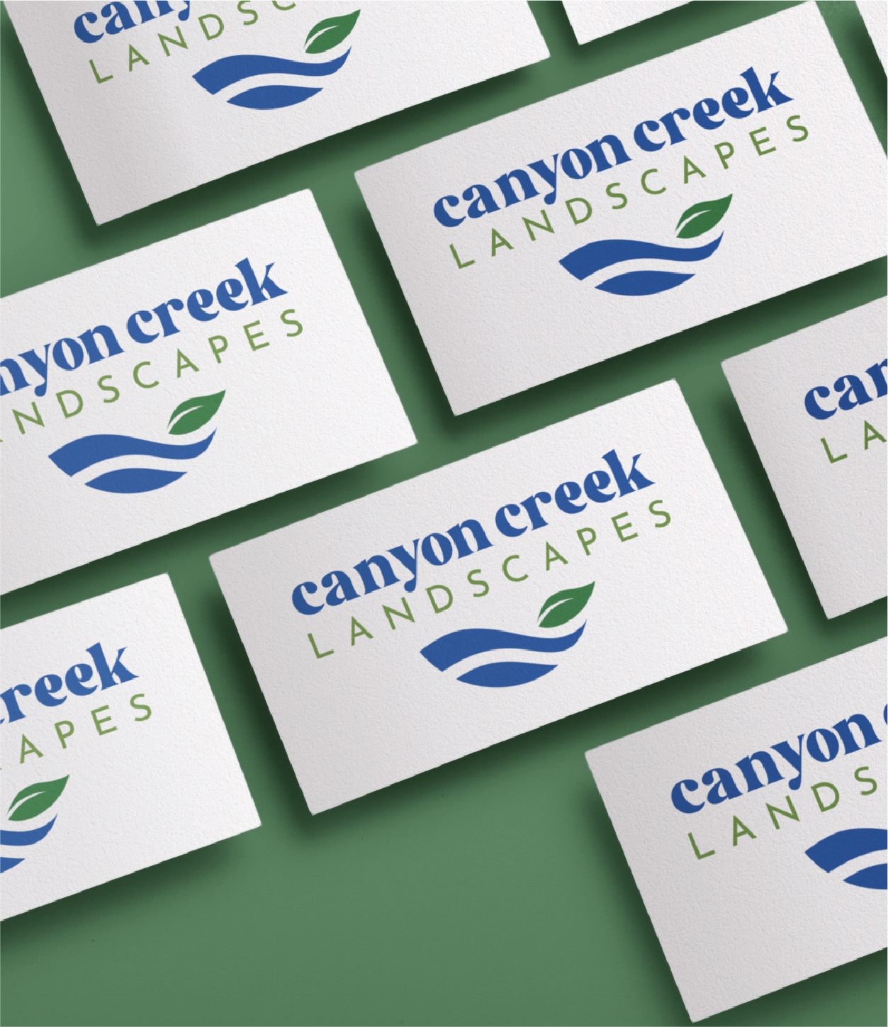 Business cards arranged on a green surface, featuring the Canyon Creek Landscapes brand design with a blue wave and two green leaves graphic. Ideal for showcasing compliance service credentials in New Jersey.