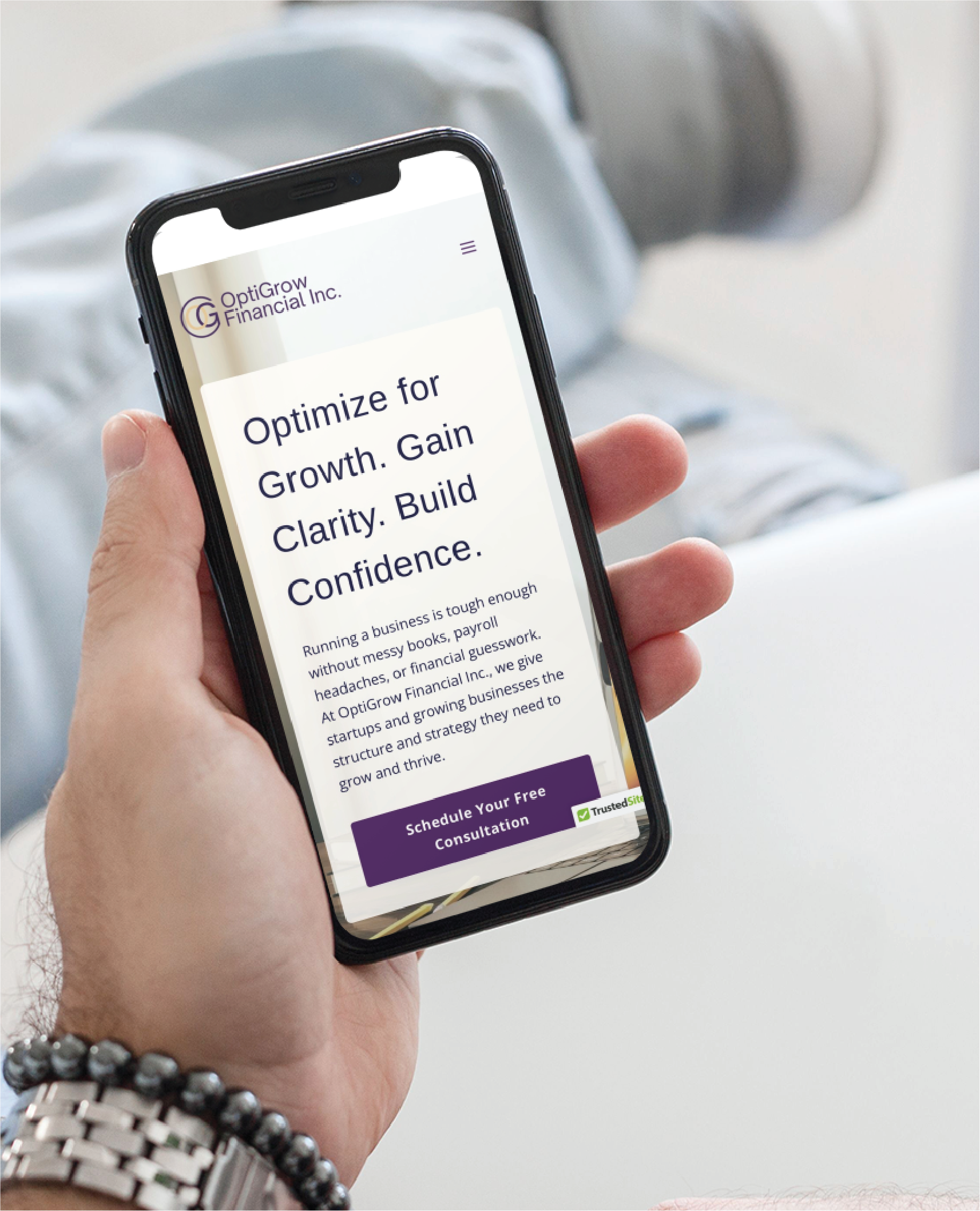 A person in Texas holds a smartphone displaying the OptiGrow Financial Inc. website, which features text about optimizing for growth, a purple button for a free consultation, and modern website design. The person wears a beaded bracelet.