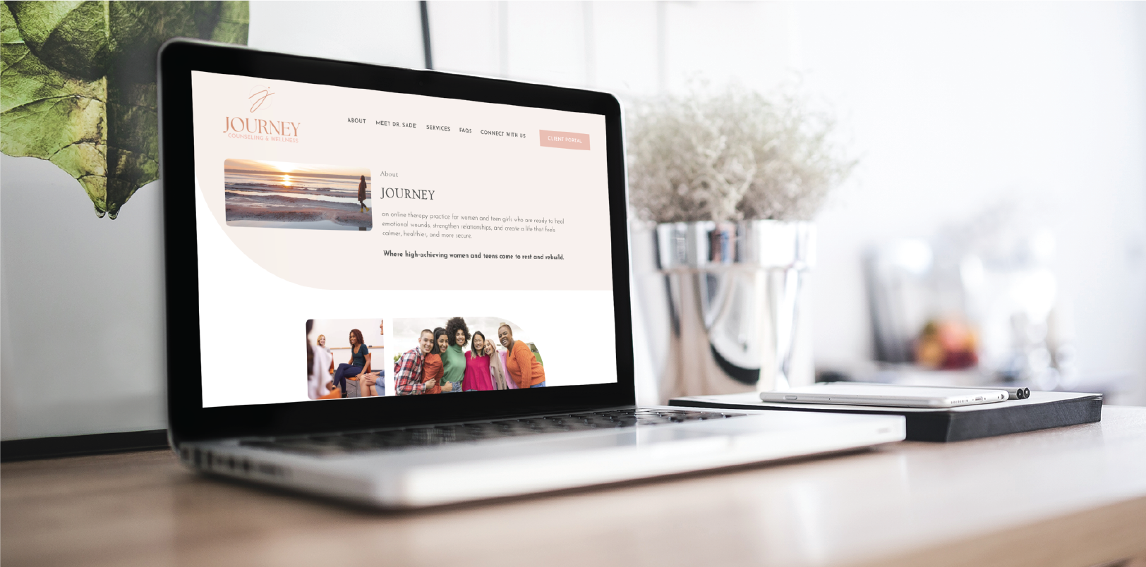 A laptop on a wooden desk displays Journey, a custom website design for counseling services in Georgia, featuring a beach sunset image, group photos of smiling people, and navigation links. A smartphone, plant, and decor are also on the desk.