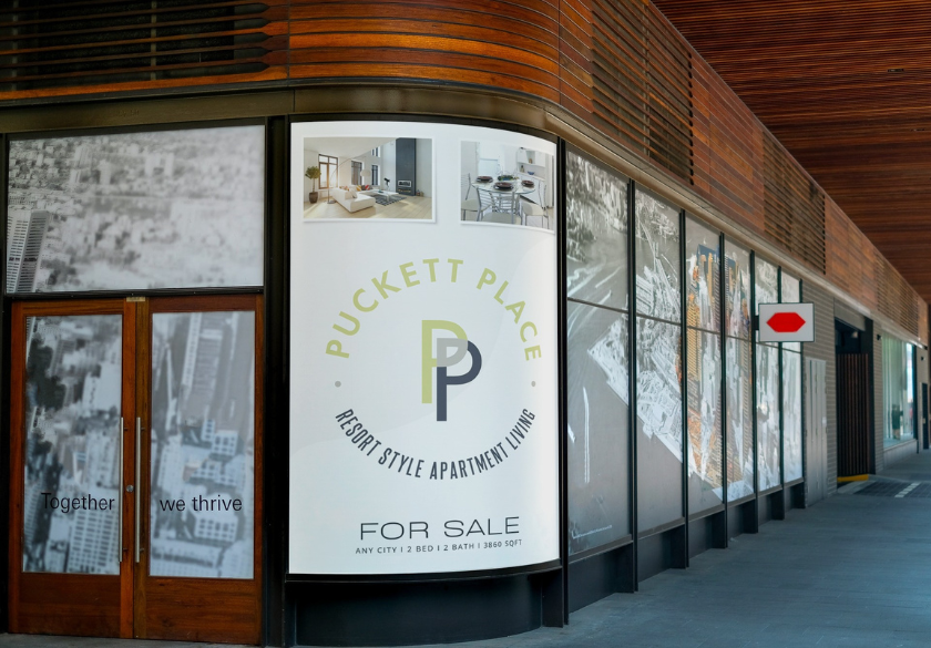 A large sign on a building advertises Puckett Place Resort Style Apartment Living and lists the property as for sale. The entrance has glass doors and city images, with text reading Together we thrive—a message that reflects the vibrant community of local businesses in the area.