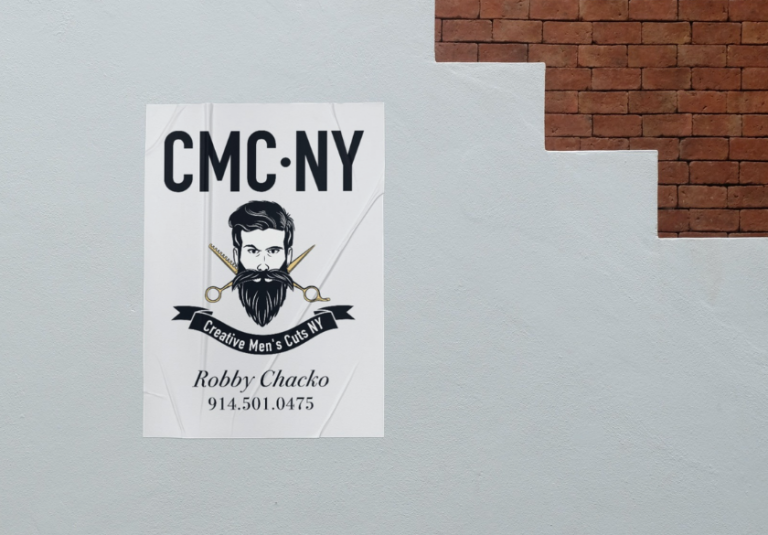 Poster on a wall for CMC NY barbershop, featuring a bearded man, scissors, and text: Creative Mens Cuts NY, Robby Chacko, 914.501.0475. Brick stairs are visible above—a standout example of print marketing designed to attract attention and support local businesses.