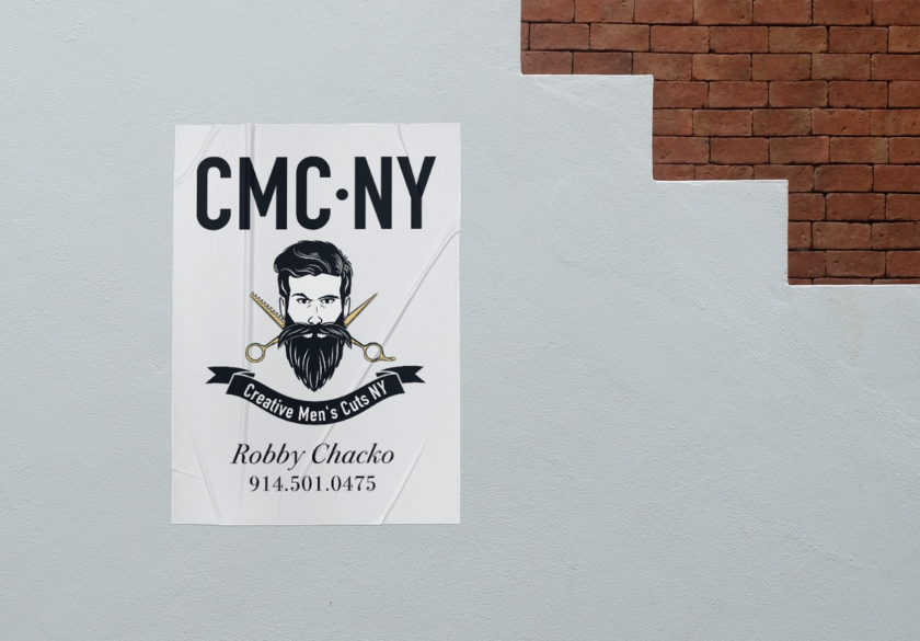 Poster on a wall for CMC NY barbershop, featuring a bearded man, scissors, and text: Creative Mens Cuts NY, Robby Chacko, 914.501.0475. Brick stairs are visible above—a standout example of print marketing designed to attract attention and support local businesses.