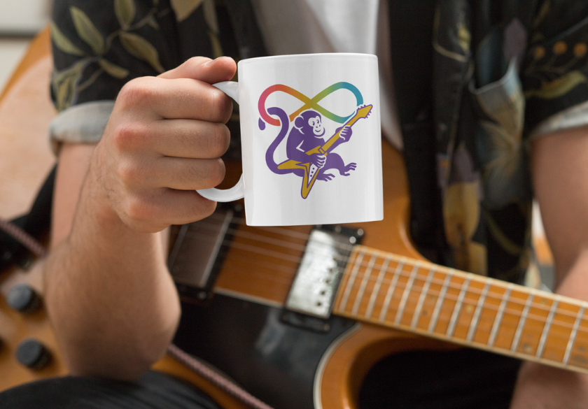 A person holds a white mug featuring a colorful monkey playing guitar—an eye-catching design perfect for print marketing pieces promoting local businesses. The person, wearing a patterned shirt, sits with an electric guitar resting on their lap.