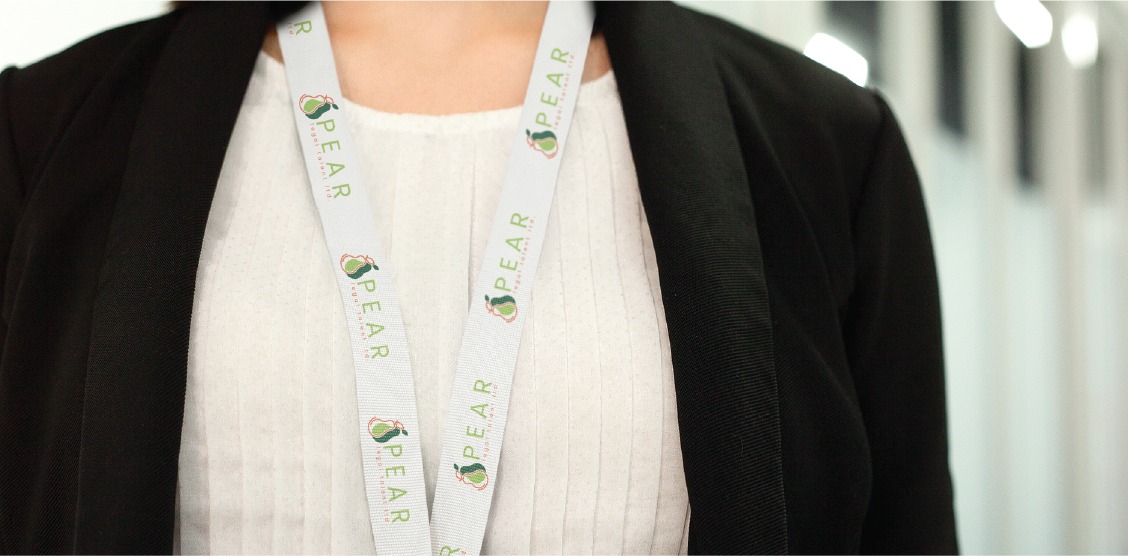 A person wearing a white blouse, black blazer, and a lanyard with the word PEAR and a pear logo stands indoors with a blurred background, representing Legal Recruitment in Toronto.
