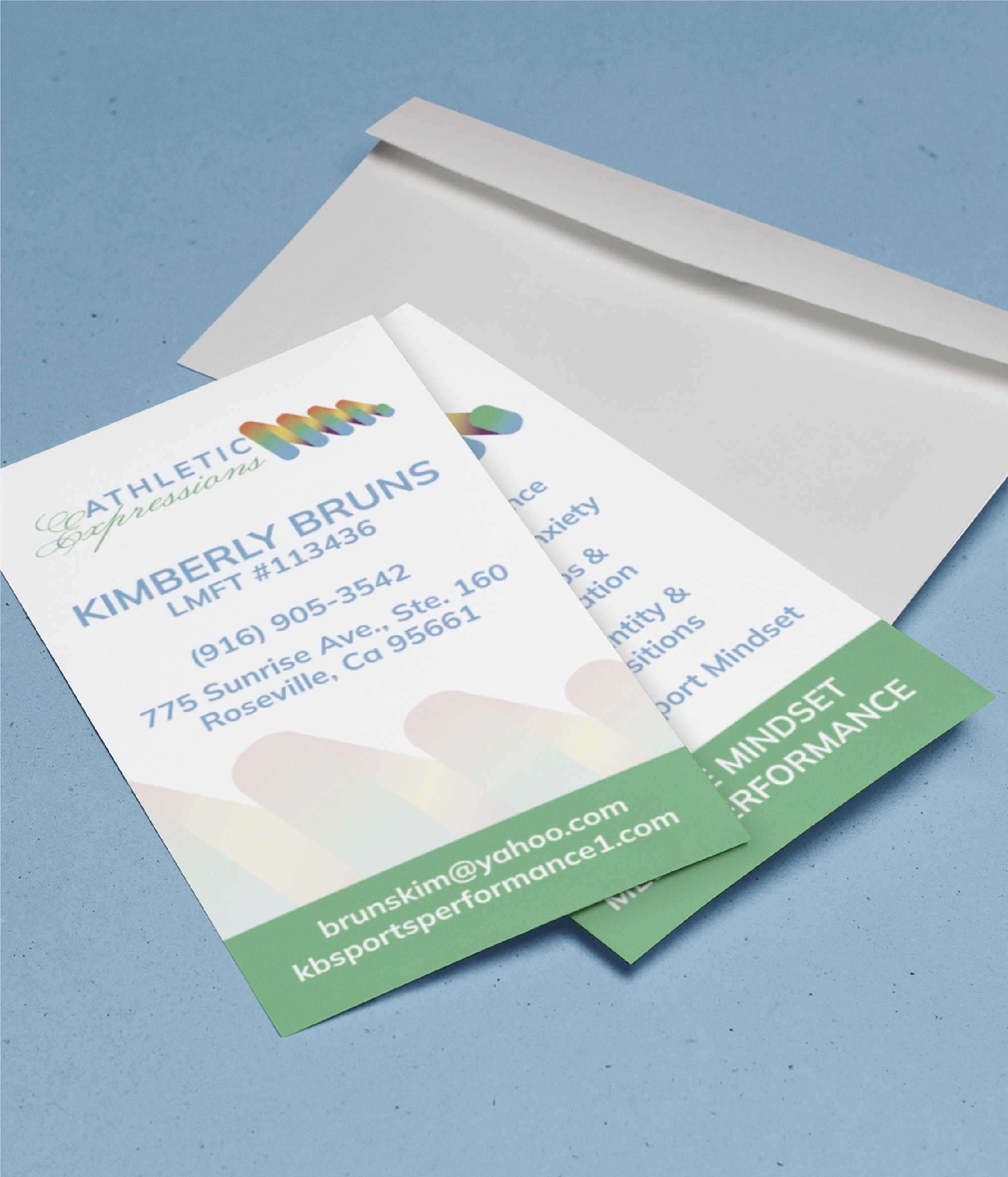 Two business cards for Athletic Expressions partly overlap on a blue surface next to an open white envelope. Showcasing professional business card design, the cards display contact info for Kimberly Bruns, LMFT in Roseville, CA, with green and blue branding—reflecting her commitment to quality business service.