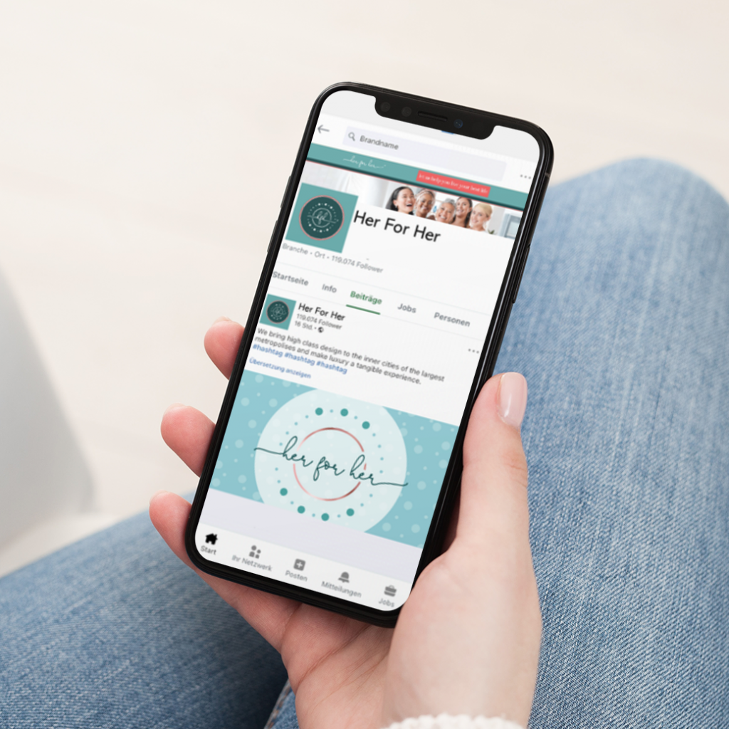 A person holds a smartphone displaying a LinkedIn profile for “Her For Her” with a teal logo and cover image, while sitting cross-legged in casual blue jeans. The profile highlights a Women's Life Coach based in California, showcasing thoughtful social media design elements throughout.