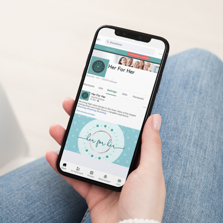 A person holds a smartphone displaying a LinkedIn profile for “Her For Her” with a teal logo and cover image, while sitting cross-legged in casual blue jeans. The profile highlights a Women's Life Coach based in California, showcasing thoughtful social media design elements throughout.
