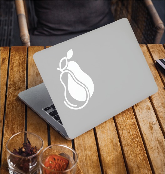 A silver laptop with a large white pear sticker on the lid sits on a wooden table in Toronto, next to two small glasses—one with dried flowers and one with orange slices—perfect for logo creation or legal recruitment brainstorming sessions.