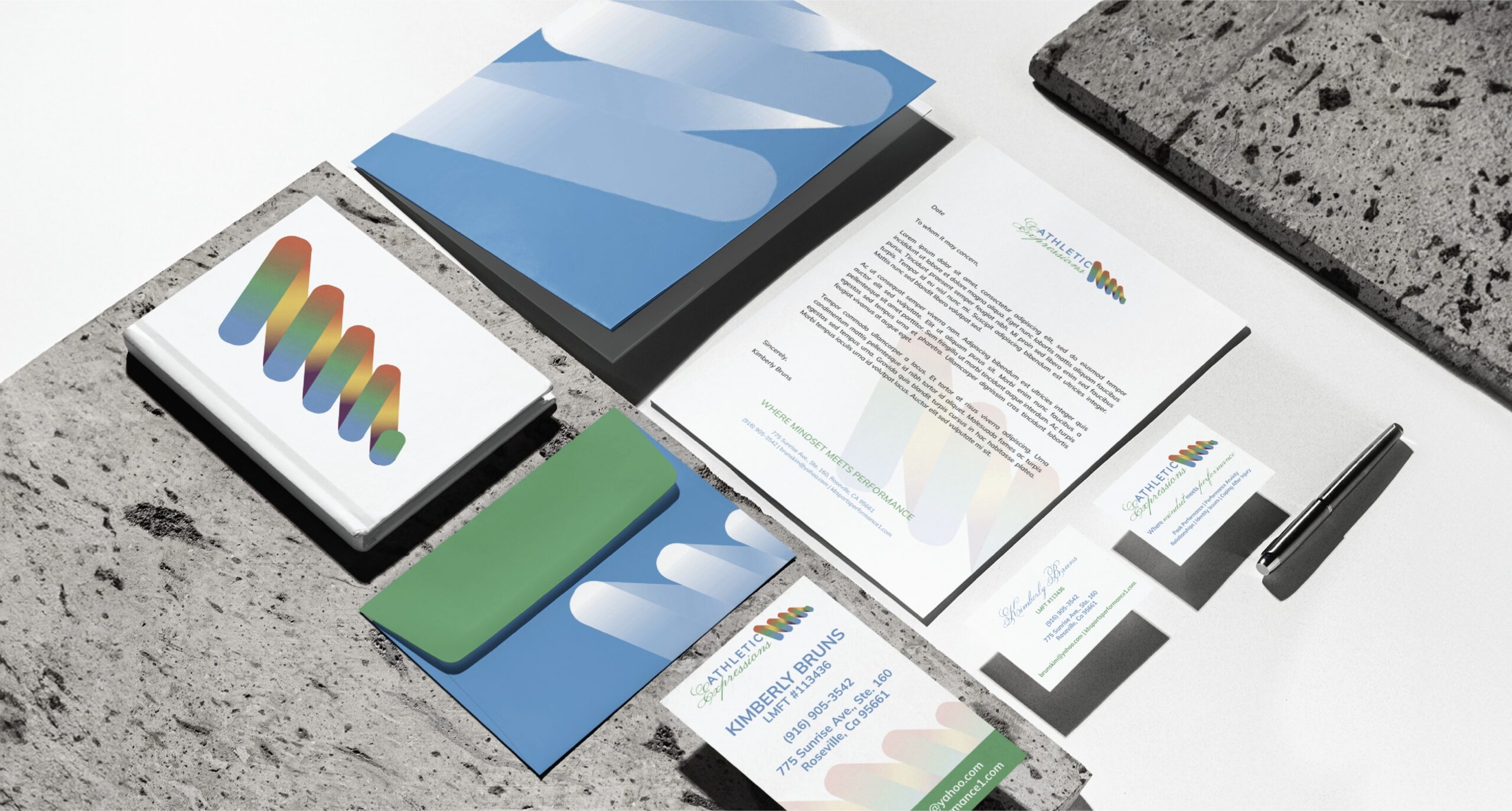 Branding materials arranged on a concrete surface, including colorful logo cards, brochures, and a pen.