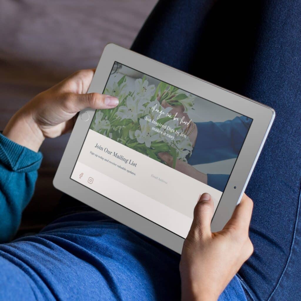 A person holds a tablet while lying down, viewing an interior designer's website featuring flowers and text inviting them to join the mailing list by entering their email address.