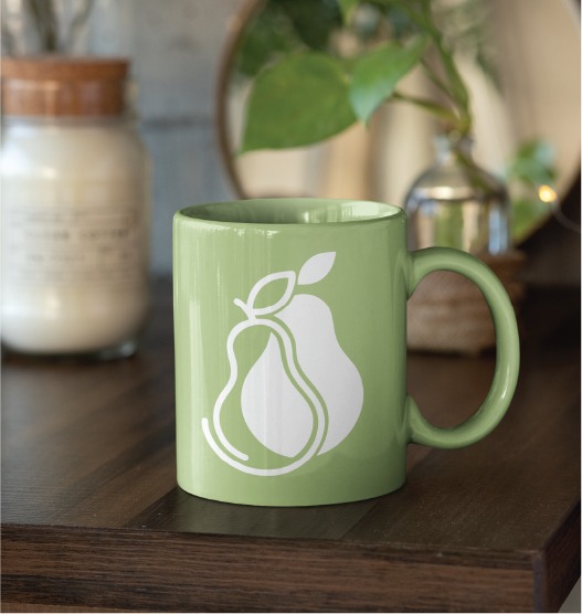 A green ceramic mug with a white pear illustration sits on a dark wooden surface, beside a candle and small plant. Perfect for clients in legal recruitment Toronto or those seeking professional logo inspiration.