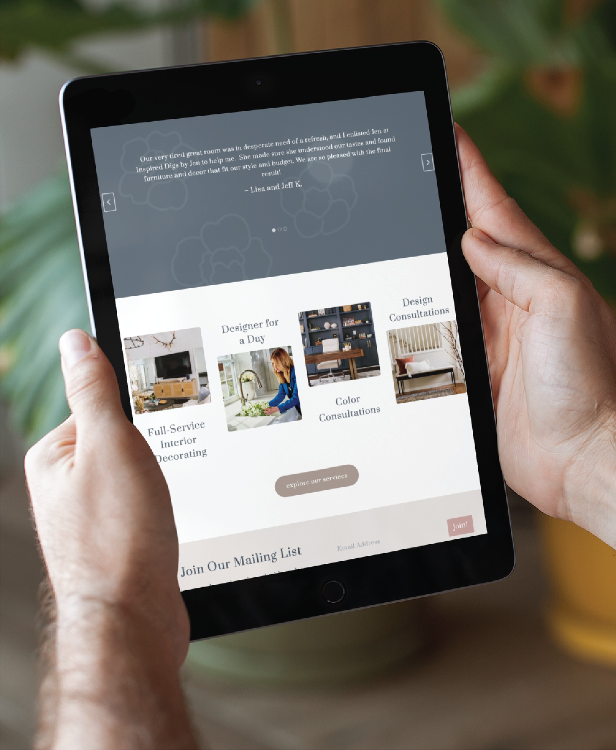 A person in Texas holds a tablet displaying an interior design website with service options like full-service decorating, web design consultations, and designer for a day. A plant is blurred in the background.