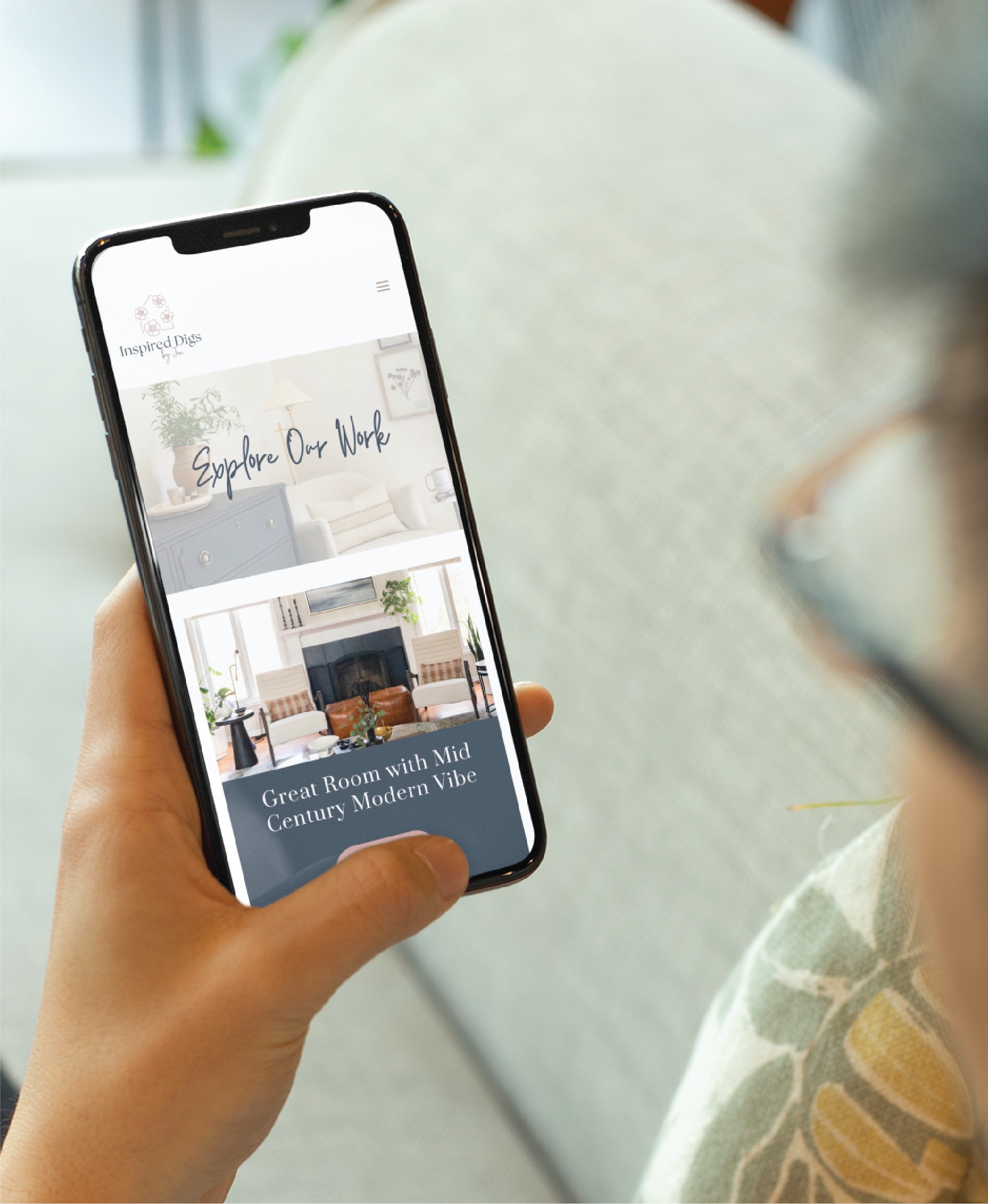 A person in Texas holds a smartphone displaying a beautifully crafted web design for a home decor website, featuring sections titled Explore Our Work and Great Room with Mid Century Modern Vibe alongside stunning interior images.
