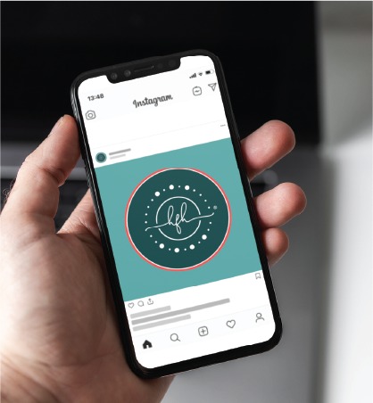 A hand holds a smartphone displaying an Instagram post with a teal circular logo featuring cursive white letters and decorative dots, showcasing the elegant social media design of a Pennsylvania skincare brand.