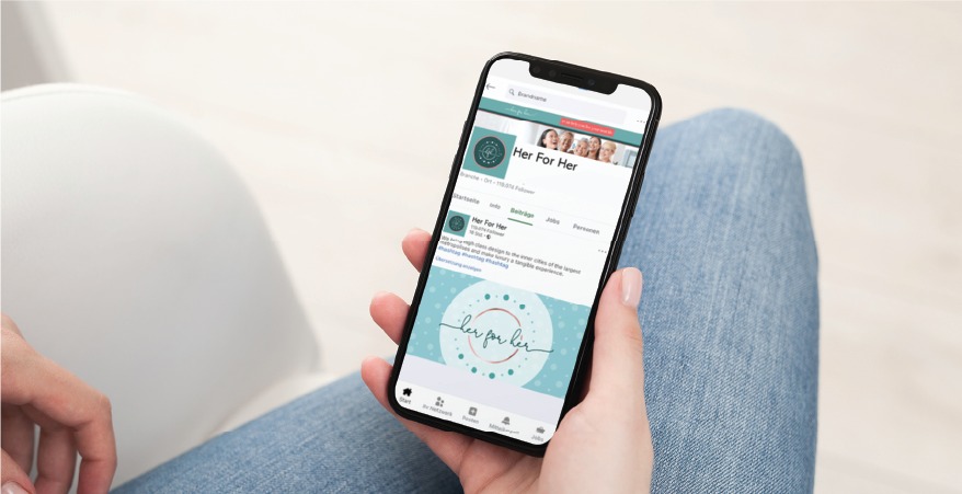 Hand holding a smartphone displaying a dating app screen with'Her For Her' branding and profile thumbnails at the top.