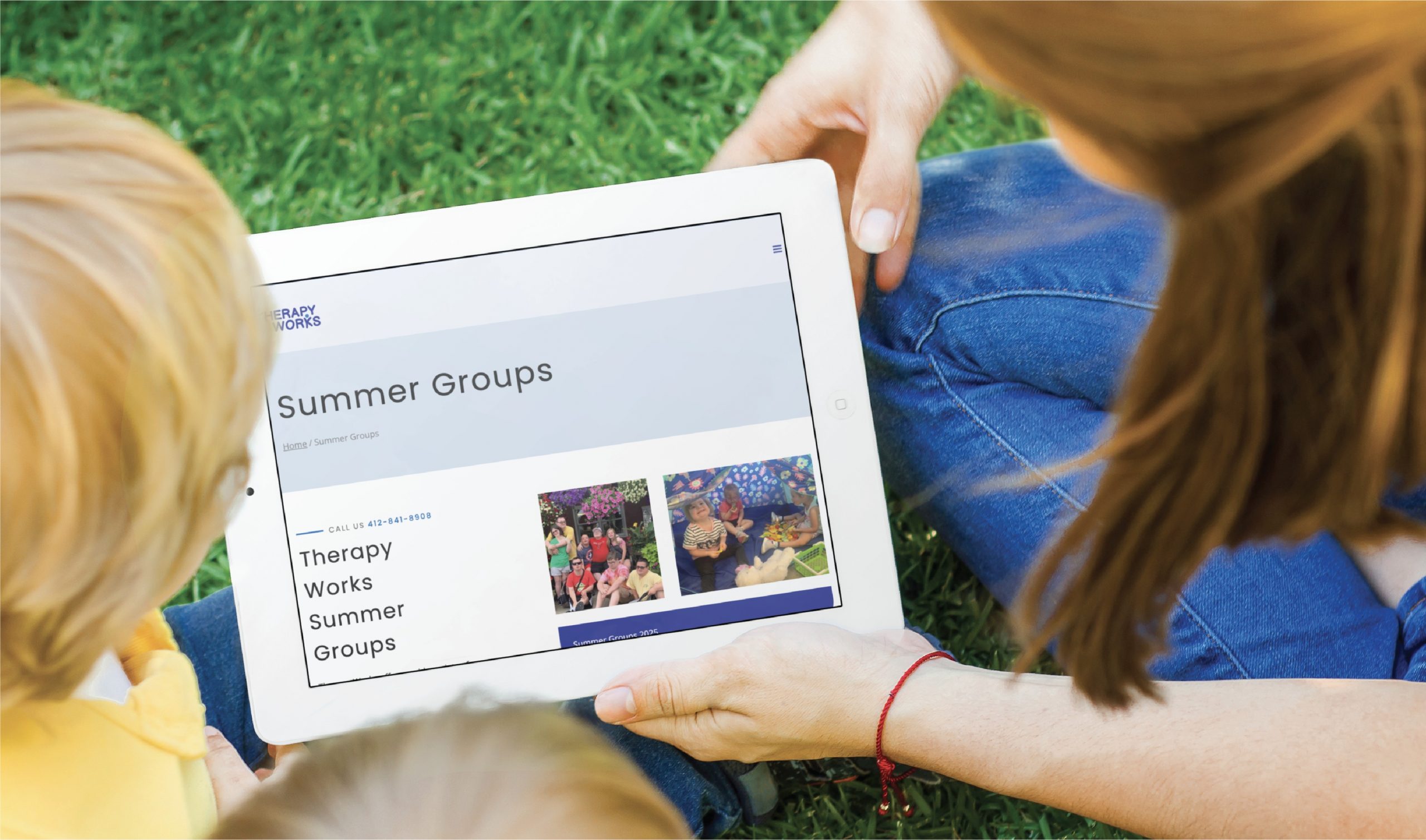 An adult and a child sit on the grass in Pennsylvania, looking at a tablet displaying a website page for Therapy Works Summer Groups, which features text and photos of children participating in youth therapy group activities, highlighting thoughtful website design.