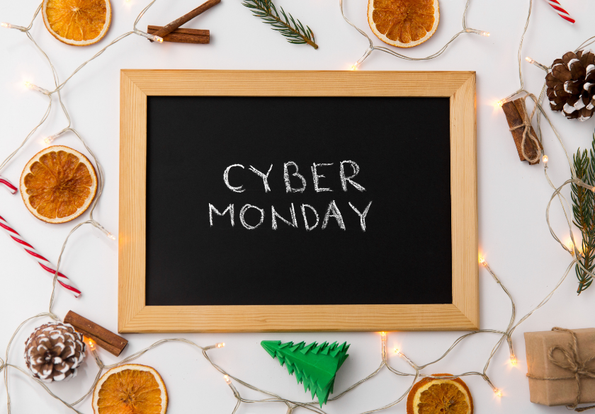 A chalkboard with CYBER MONDAY written on it, surrounded by dried orange slices, pinecones, cinnamon sticks, fairy lights, a candy cane, and a green paper tree on a white background—perfect for inspiring Holiday Marketing ideas for your Small Business Website this Q4.