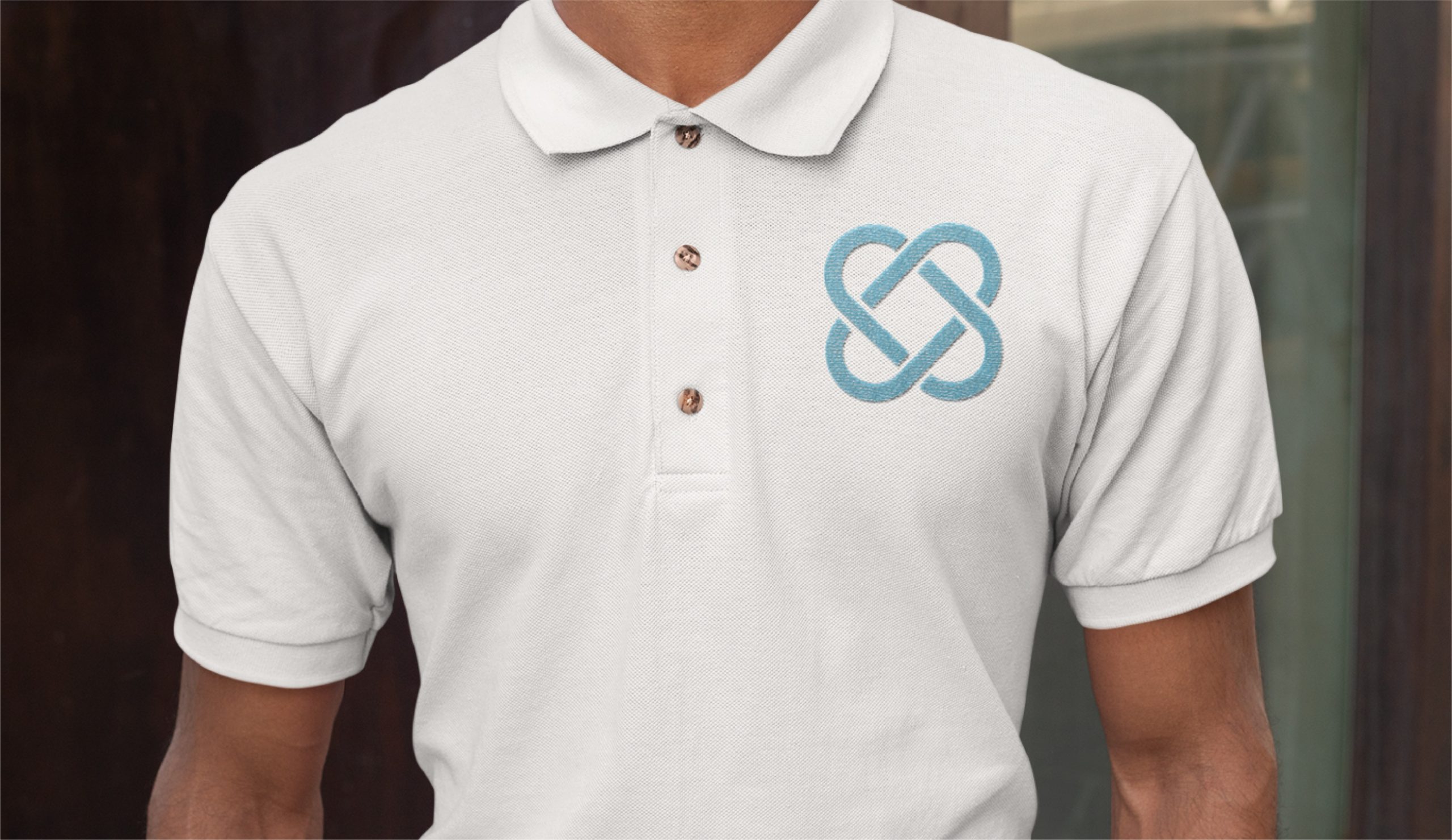 Person wearing a white polo shirt with three buttons and a blue intertwined logo on the left chest, standing in front of a dark background—a polished look favored by Texas-based IT consultants who appreciate smart logo design.