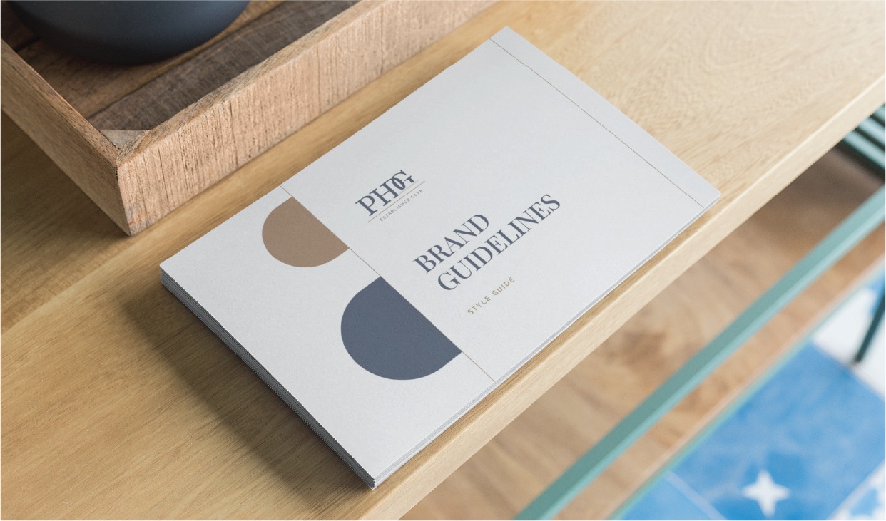 A booklet labeled PHOX Brand Guidelines: Style Guide lies on a wooden shelf, featuring minimalist beige, blue, and brown design elements on its cover—an inspiring example of sophisticated Stationery Design perfect for businesses in Ohio.