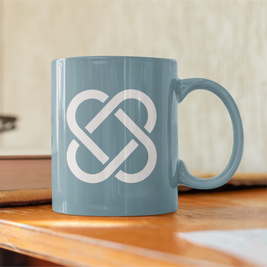 A blue mug with a white, intertwined loop logo design sits on a wooden surface, with a blurred background.