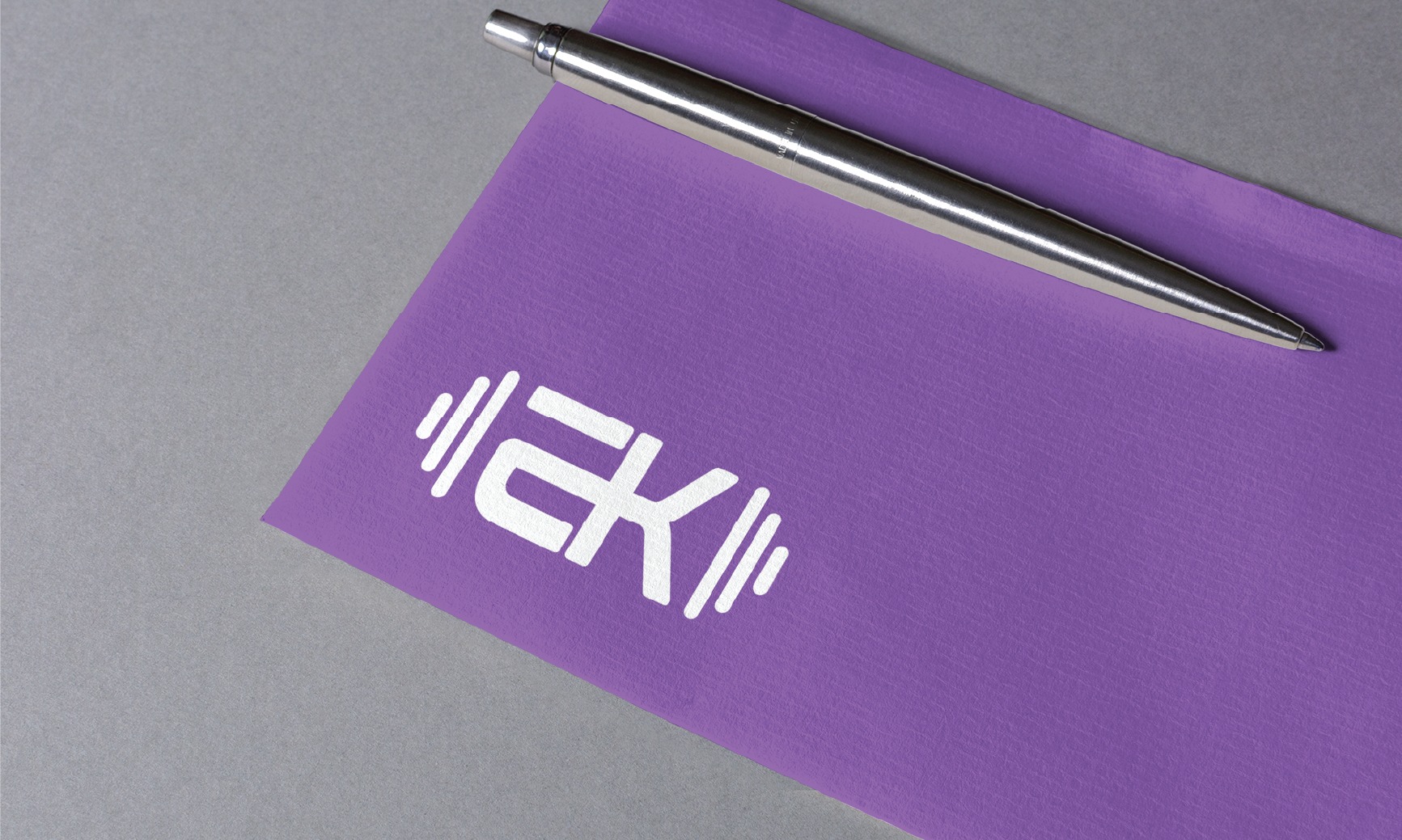 Purple notebook with a white geometric logo and a silver pen resting on it against a gray background.