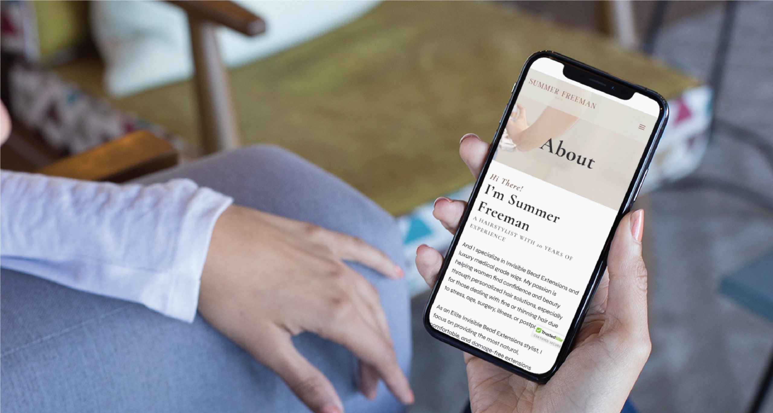 A person holds a smartphone displaying a website’s About page introducing Summer Freeman, a Colorado-based Spiritual Therapist, while sitting on a couch with their hand resting on their knee.