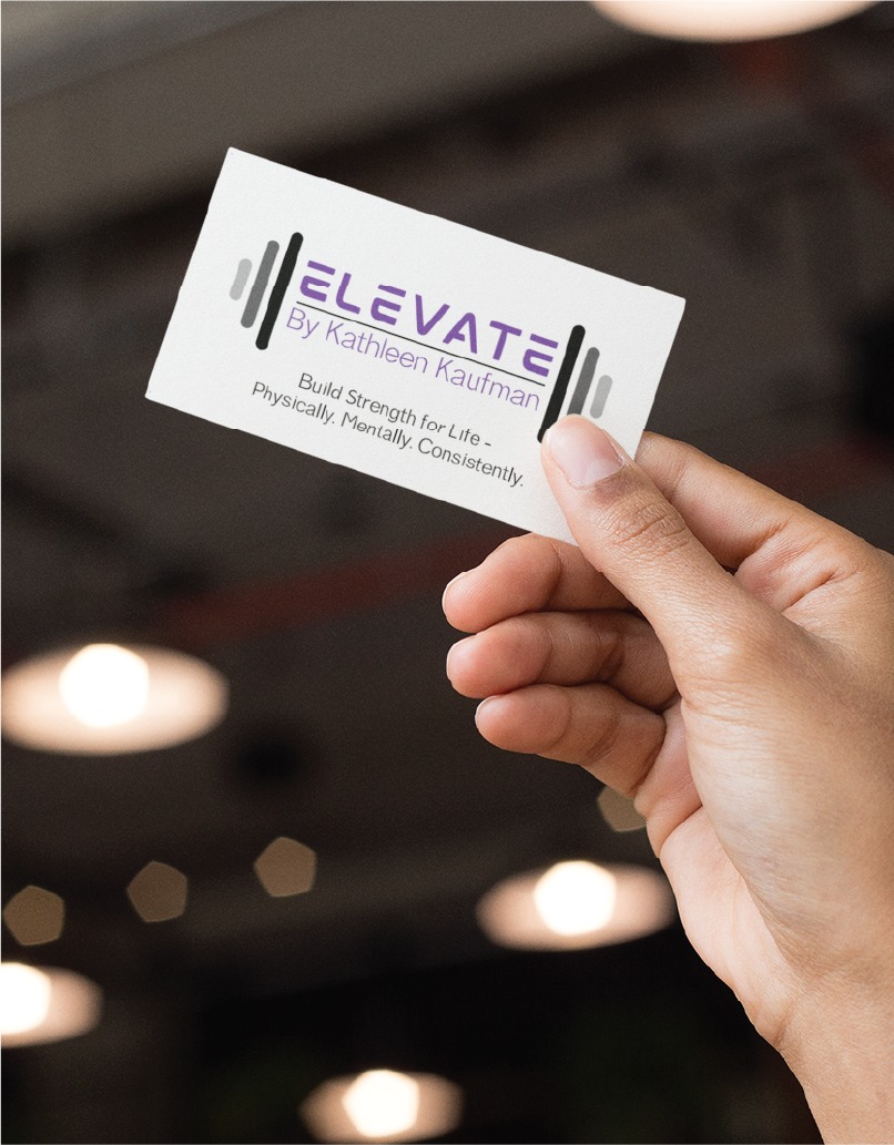 Close-up of a hand holding a business card that reads'ELEVATE by Kathleen Kaufman' with the tagline 'Build Strength for Life – Physically. Mentally. Consistently.'