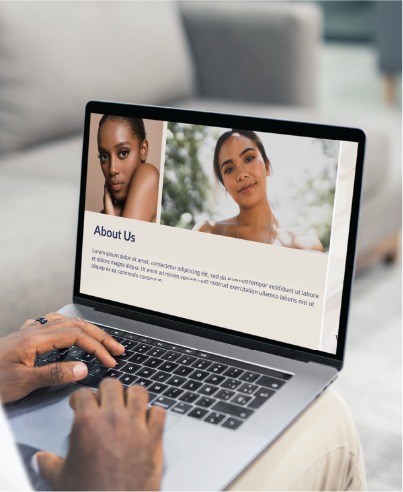 A person types on a laptop displaying an About Us page with photos of two women and placeholder text, while sitting on a couch—highlighting an Indiana-based accounting service’s expertise in social media design.