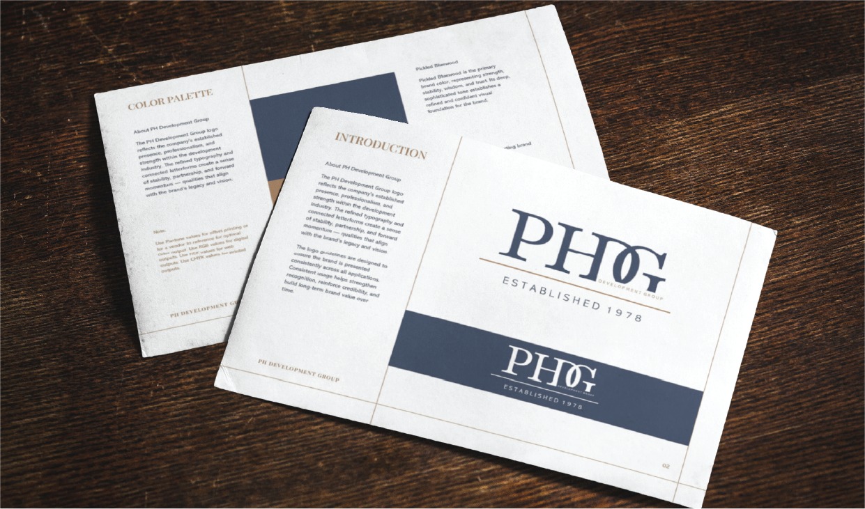 Corporate brochure spread on a dark wooden desk, featuring white pages with navy blue panels and the PHG logo (Established 1978).