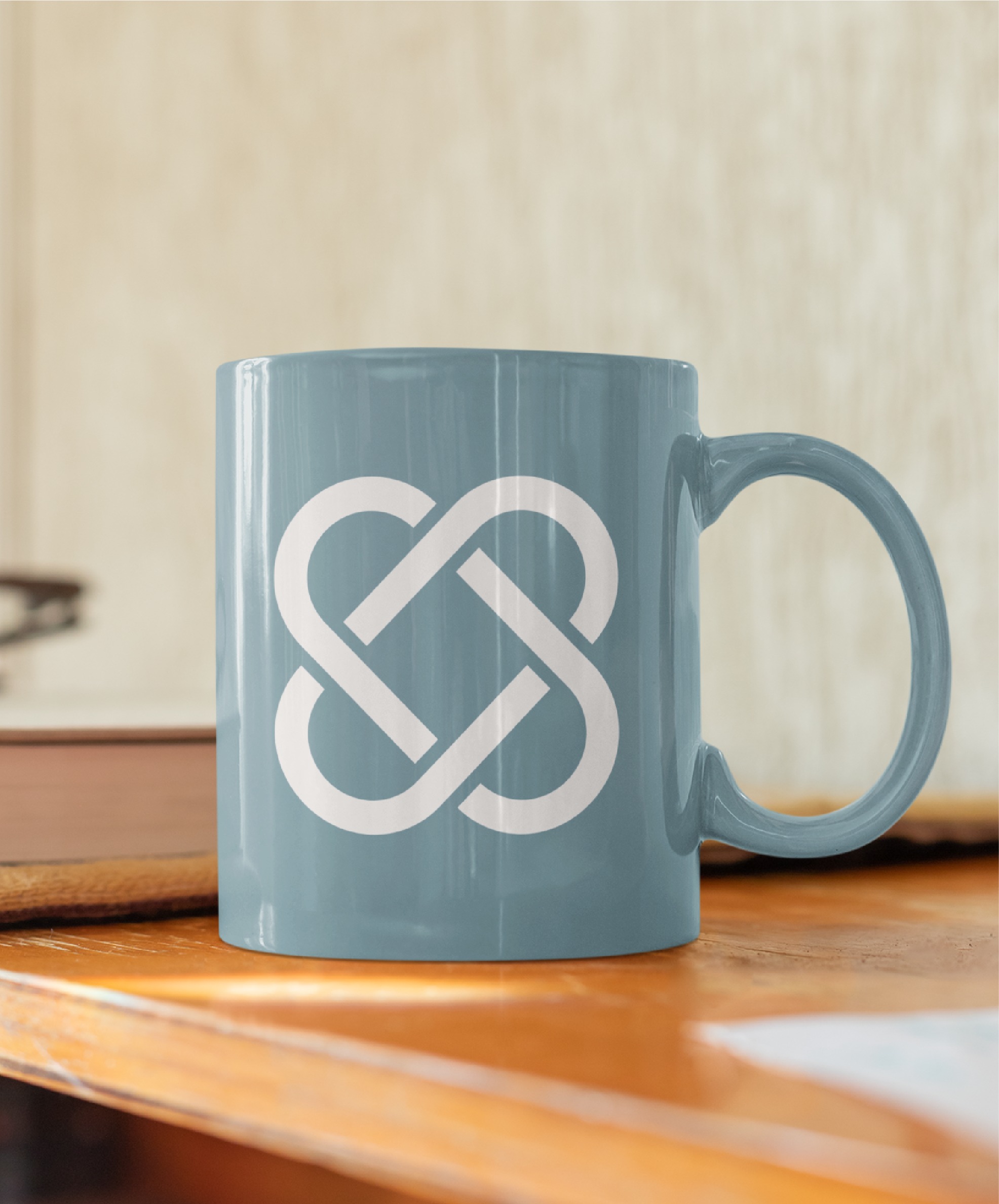 A blue ceramic mug with a white geometric knot design—reminiscent of modern logo design—sits on a wooden surface near a closed book and a sheet of paper, evoking the creative workspace of IT consultants in Texas.