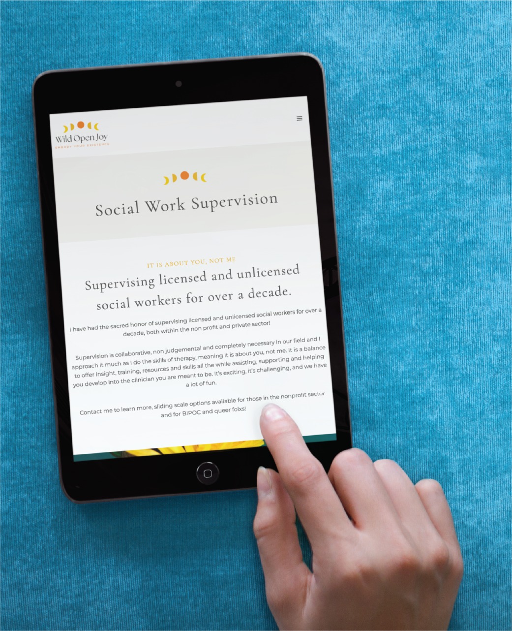 A hand holds a tablet displaying a webpage about social work supervision services in Colorado, highlighting over a decade of experience supervising licensed and unlicensed social workers. The tablet rests on a textured blue surface.