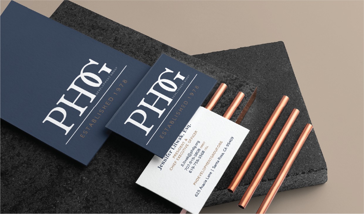 Navy branding cards with a white logo on a dark stone surface, beside copper pens. Readable but concise.
