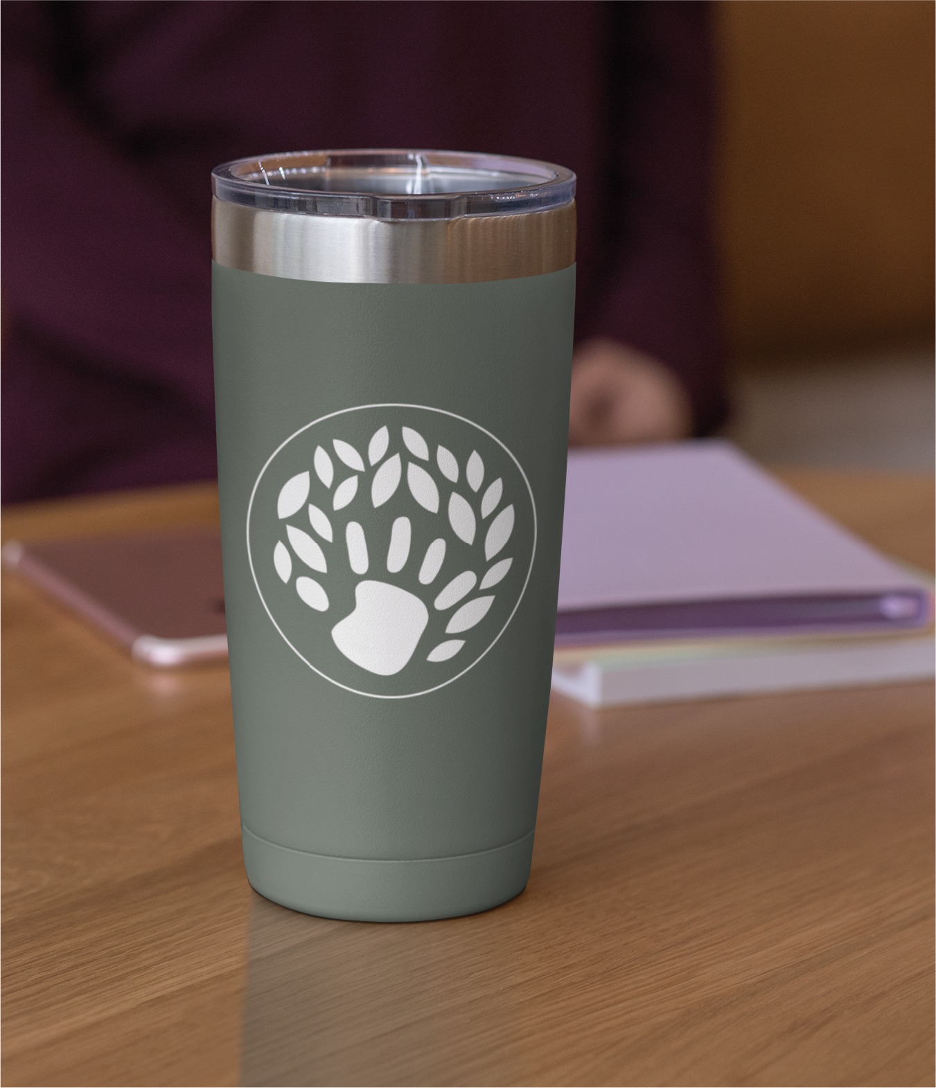 Grey-green insulated tumbler with a white circular logo of a paw surrounded by leaves, on a wooden desk.
