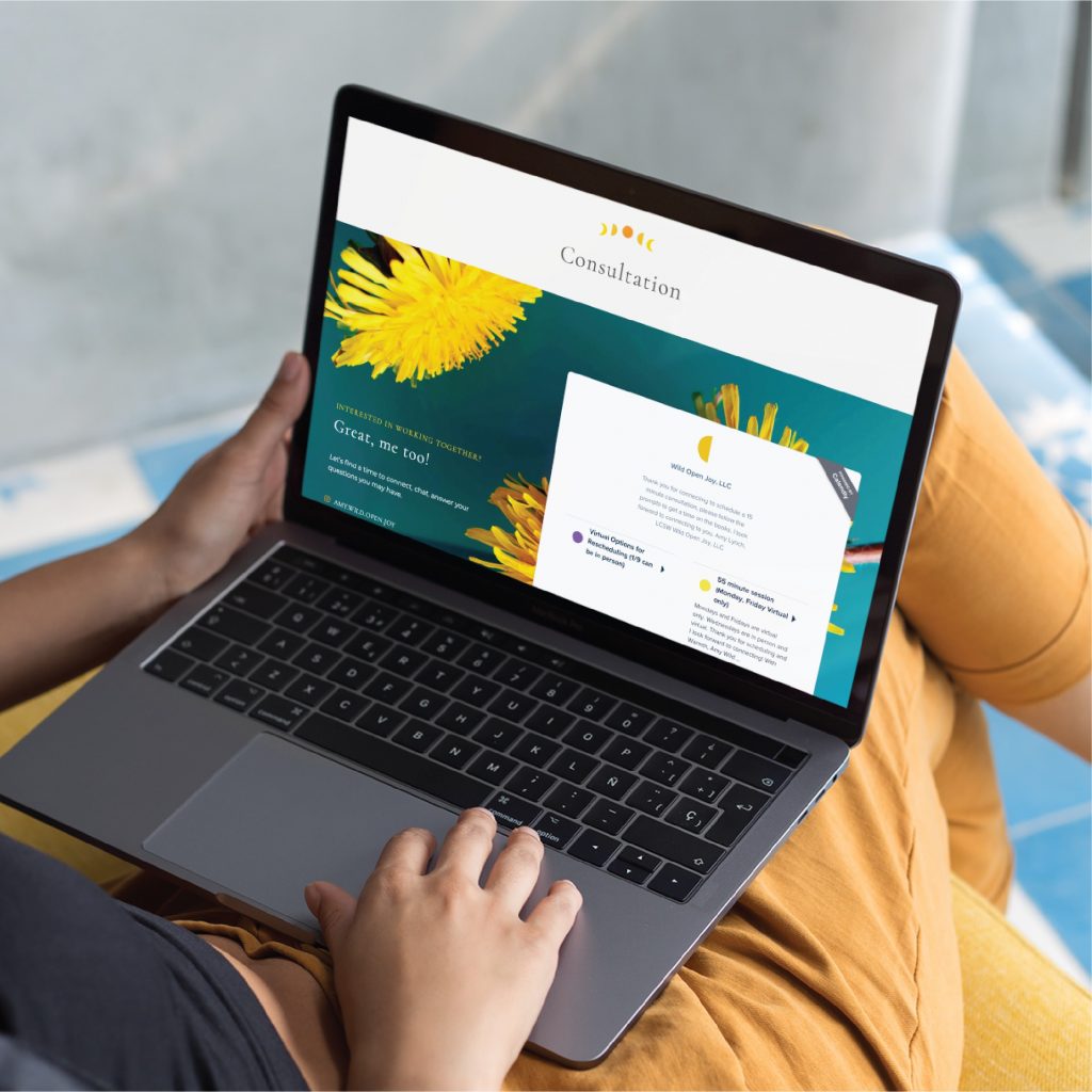 Person holding a laptop on their lap, viewing a spiritual therapist consultation webpage featuring yellow dandelion flowers and text, sitting on a yellow chair with blue and white flooring visible—a calming website design inspired by Colorado’s natural beauty.