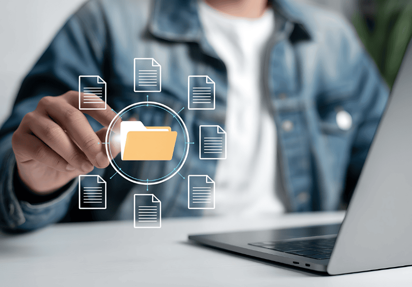 A person in a denim jacket uses a laptop and touches a virtual folder icon surrounded by document icons, symbolizing organized digital file management—an essential practice for small business owners handling valuable brand assets.