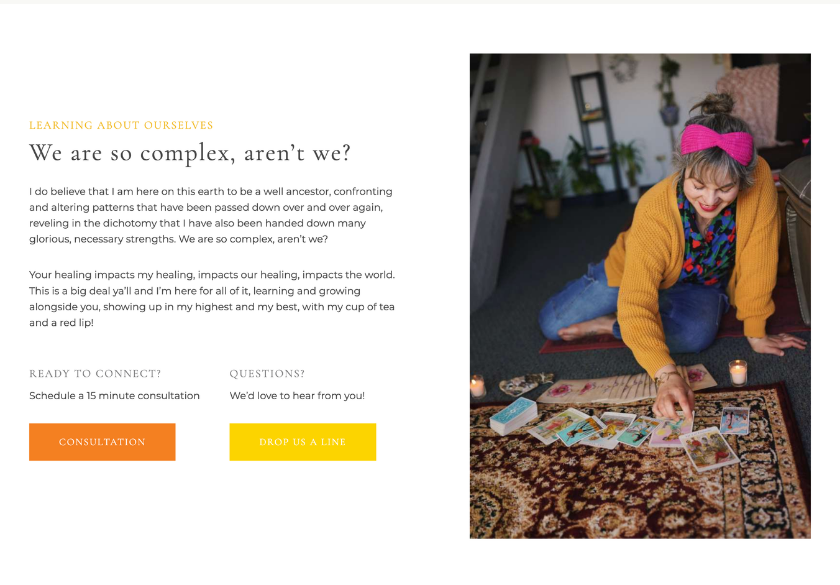 A woman with a pink bow and yellow sweater sits on the floor, smiling as she lays out tarot cards on a small table. Candles, plants, and cozy decor surround her in a warmly lit, inviting room—an atmosphere that radiates comfort and website trust, much like finding reliability in an online space you can truly relax in.