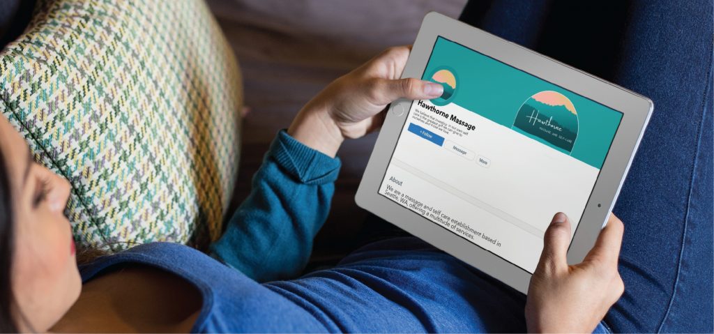 A person holding a tablet and viewing a Facebook business page for Handsome Massage, a Pennsylvania-based skincare brand, which features a teal banner with a sun and mountain logo and professional social media design.