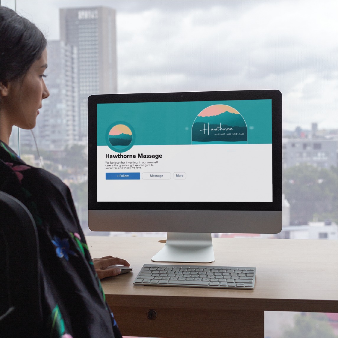 A woman sits at a desk looking at a computer screen displaying the Hawthorne Massage social media page, showcasing its sleek social media design. The cityscape of Pennsylvania is visible through the window in the background.