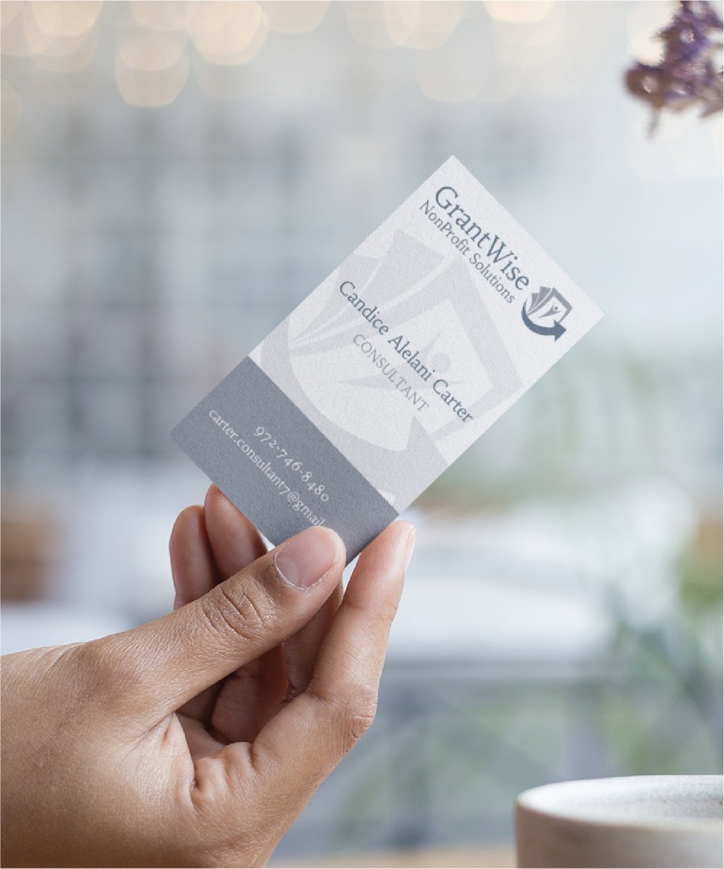 A hand holds a business card for GrantWise Nonprofit Solutions, featuring the name Candice Alain-Carter, Consultant, with contact information visible. Showcasing refined print design, the card highlights expertise in Move Management for organizations across Pennsylvania. The background is softly blurred.