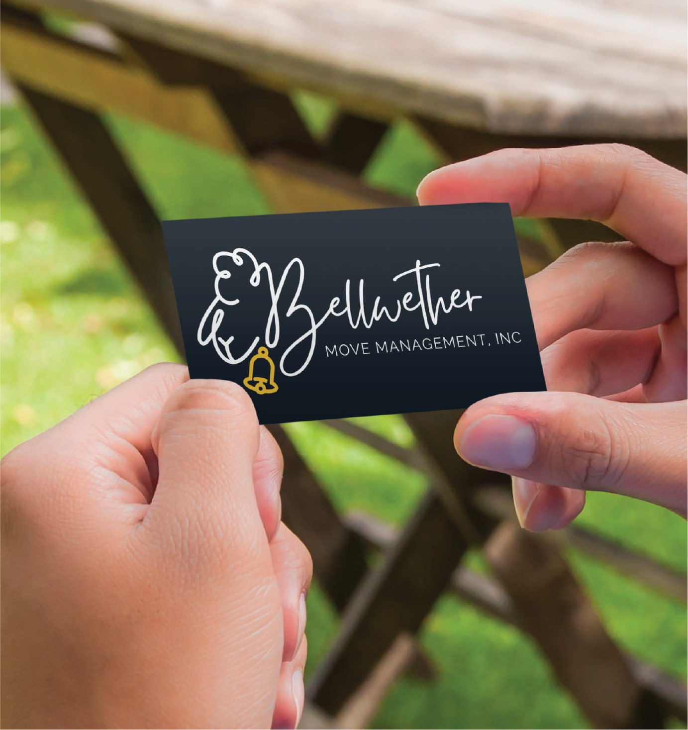 A person holds a business card that reads Bellwether Move Management, Inc., featuring a bell and sheep logo, outdoors near a wooden table. The custom print design highlights the professional move management services offered in Pennsylvania.