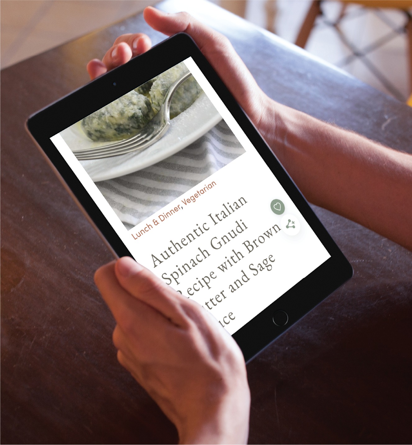 A person holds a black tablet displaying a recipe page for Authentic Italian Spinach Gnudi, showcasing the benefits of custom website design for the home cook. A fork and green dumpling are visible at the top, while the person sits at a table with a striped cloth, enjoying culinary inspiration from California.
