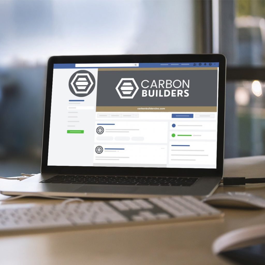 A laptop displays a company social media profile for Carbon Builders, a Full Service Contractor in Michigan, featuring a hexagon logo, on a desk with a white keyboard and papers nearby—a perfect example of custom social media design.