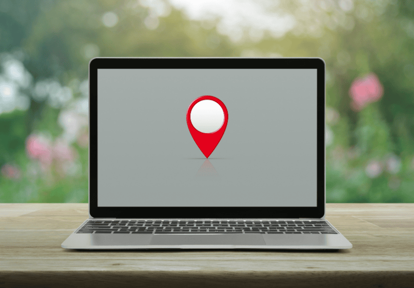 A laptop on a wooden table displaying a red map location pin, representing service area pages for local SEO.