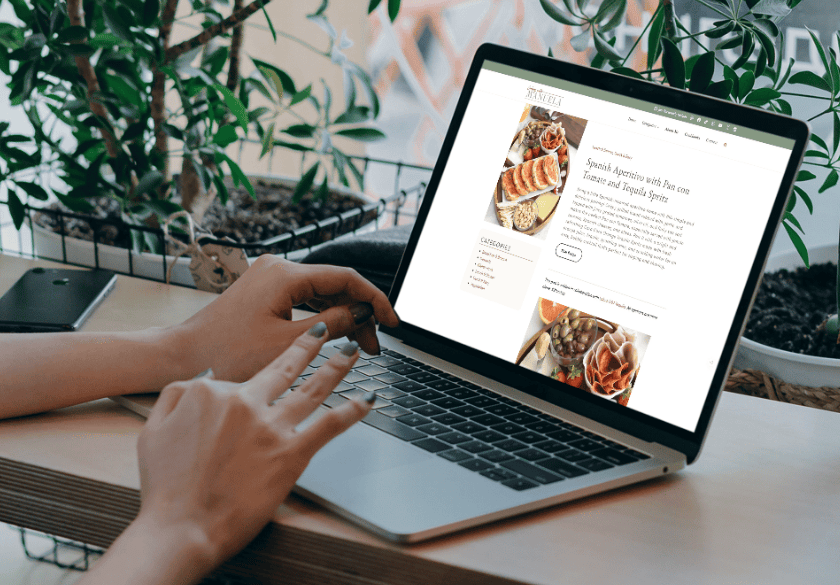 A person uses a laptop to view a food blog post titled Spanish Aperitivo with Pan con Tomate and Tequila Spritz, highlighting how high-quality content supports an effective SEO strategy.